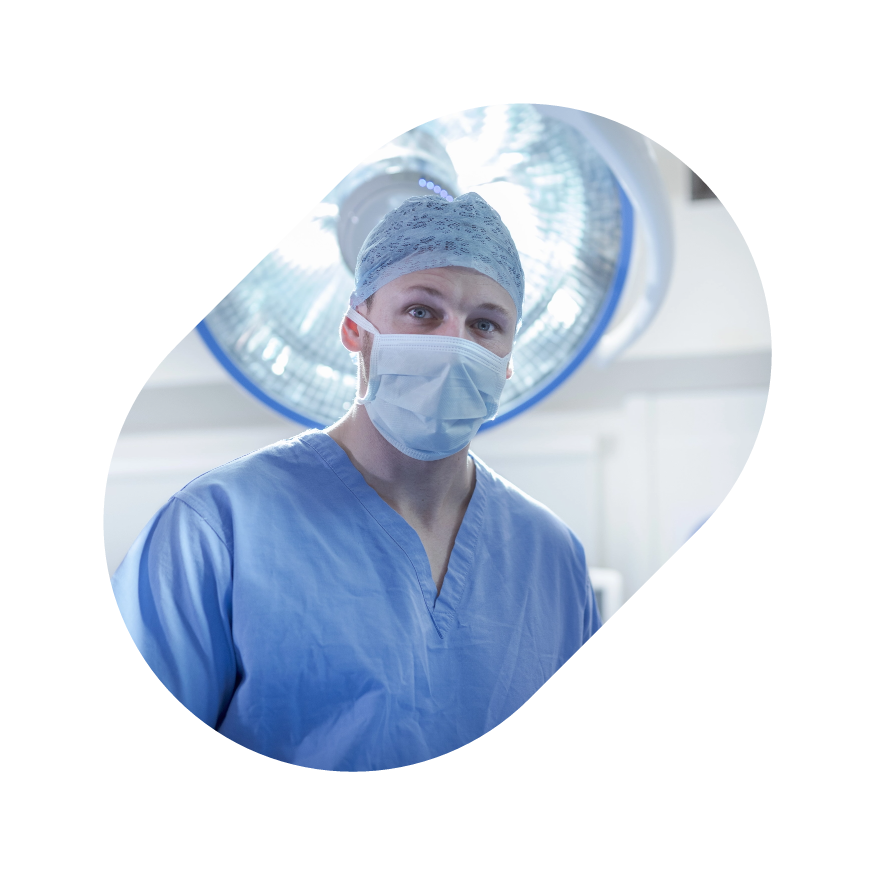 Surgeon in blue scrubs and mask under bright operating room lights.