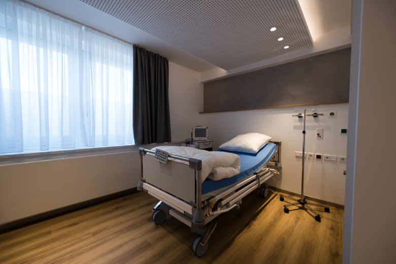 Hospital patient bed on wheels in a quiet room, blue sheets, and an IV pole beside the bed.